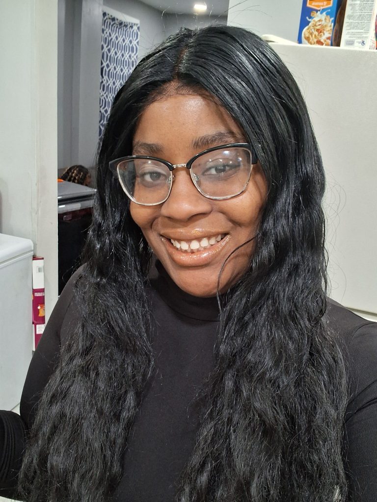 Portrait of the founder wearing glasses in a kitchen setting, with a subtle glimpse of the living room and part of the fridge in the background, creating a natural, intimate feel that reflects the calm and modern self care aesthetic of Scented Luminescence(LUMI).