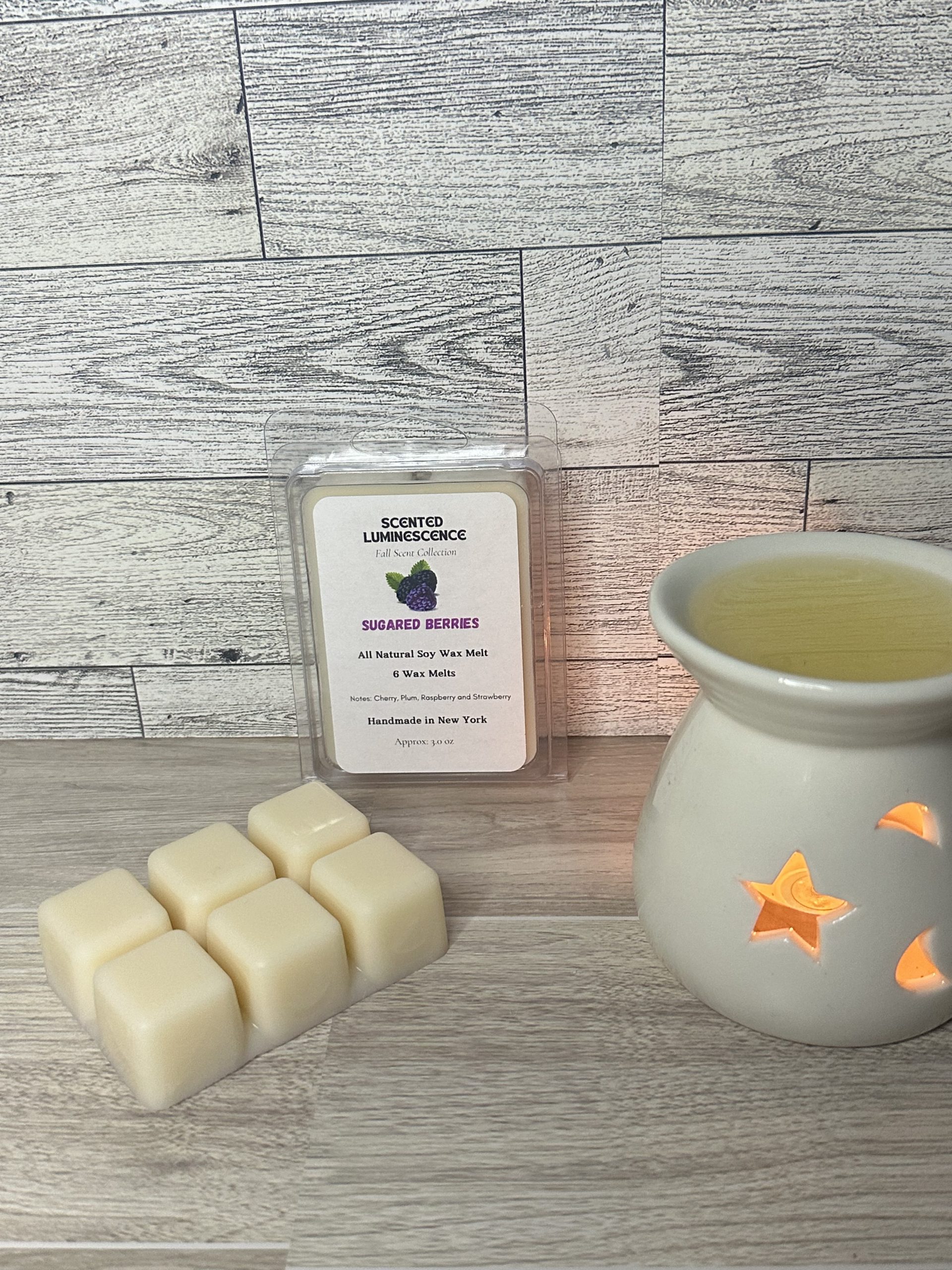 Close up of “Sugared Berries” wax melt styled on a clean background with a wax warmer and a clamshell subtly placed in the background highlighting the cozy ambiance